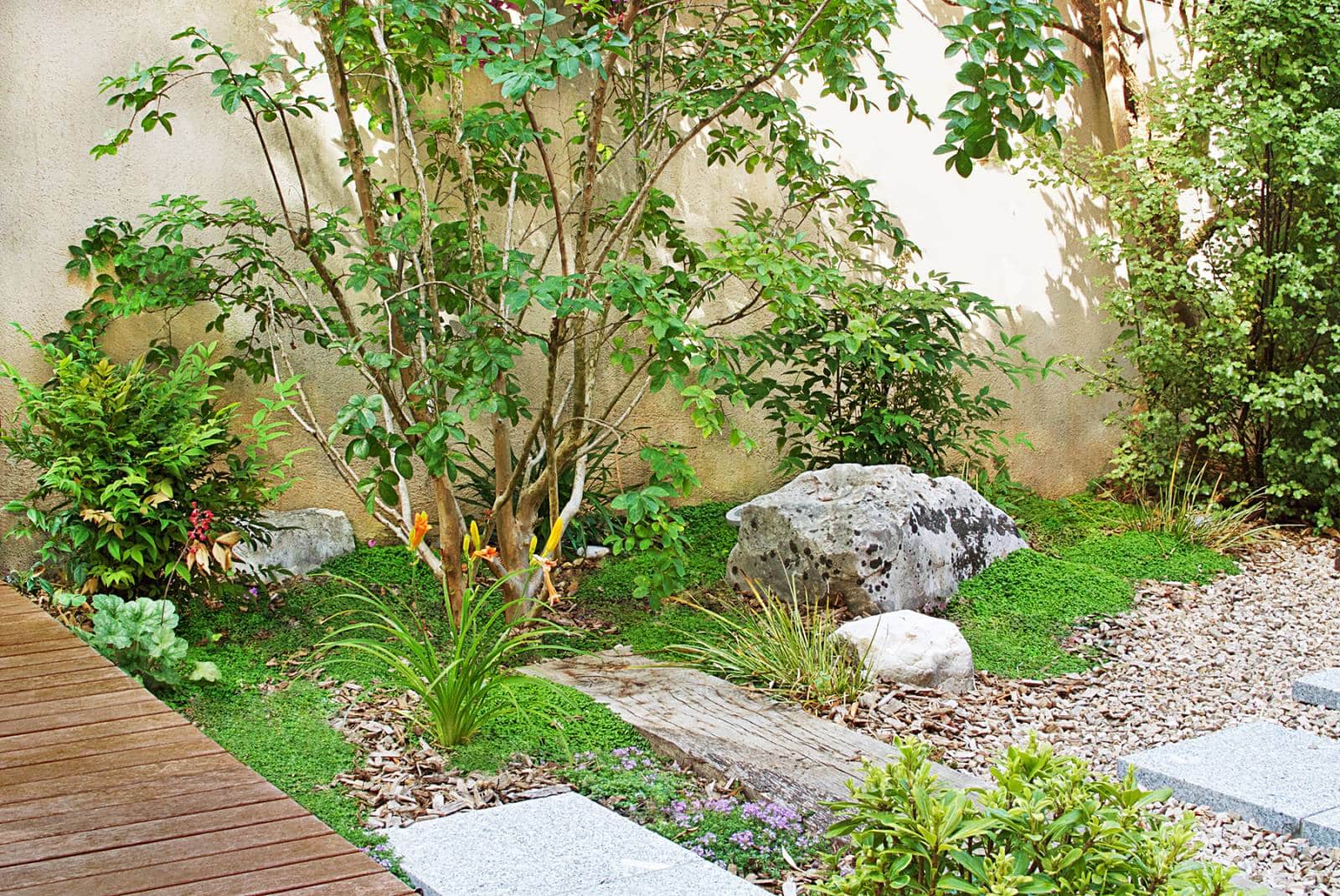 Jardin zen contemporain avec bois, gravier, pierres et feuillage luxuriant. Chemin de bois et pas japonais.